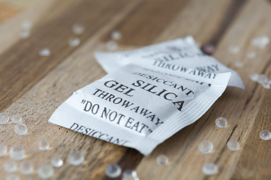 Desiccant or silica gel in white paper packaging and spread on the wooden background.