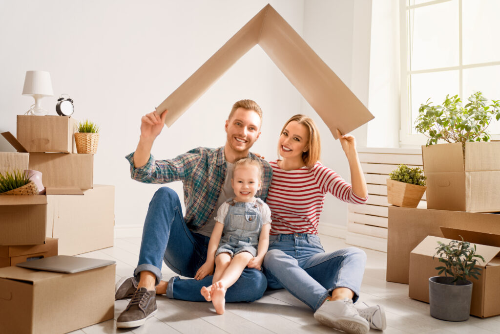 Concept of housing for young family. Mother, father and child girl in new house with a cardbox roof. Symbol of protection and property.