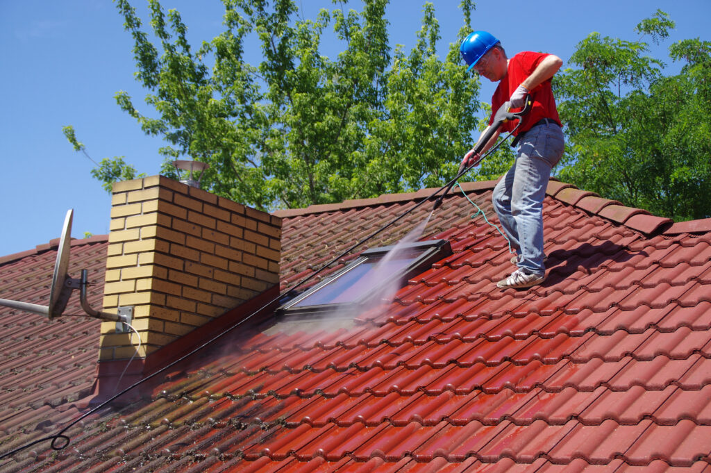 House roof cleaning with pressure tool. Worker on top of building washing tile with professional equipment. Moss removing with water.