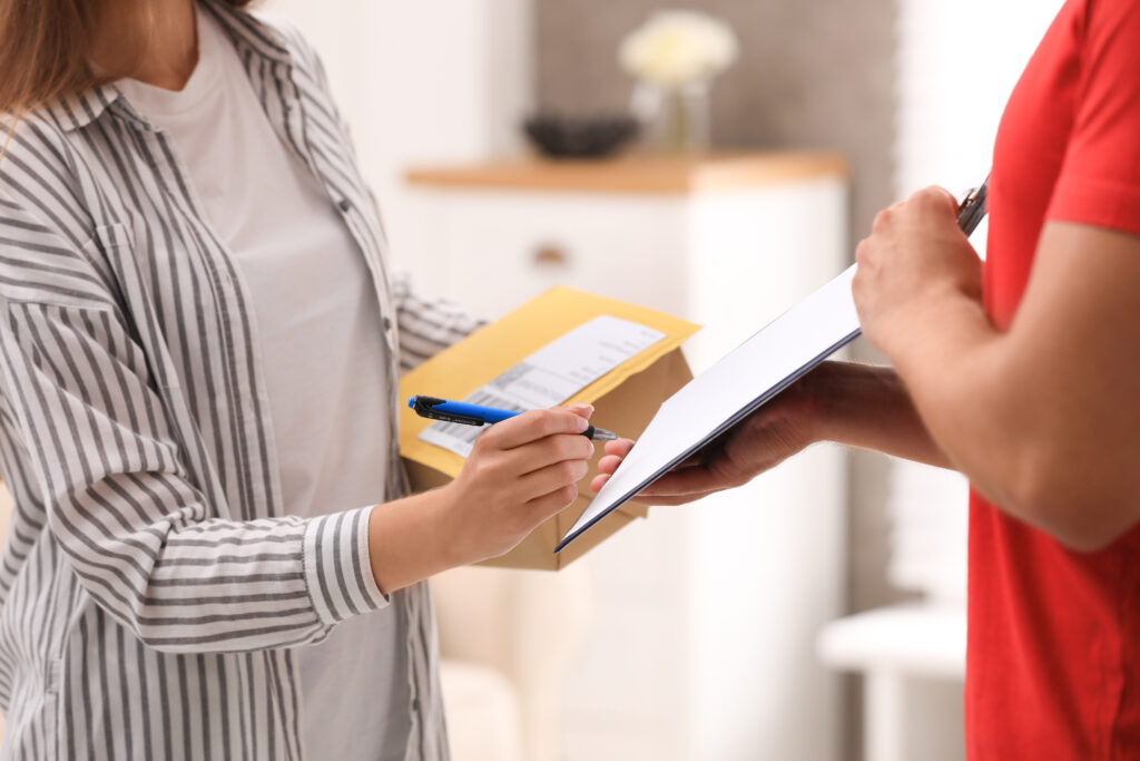 Woman signing for delivered parcels at home, closeup. Courier service