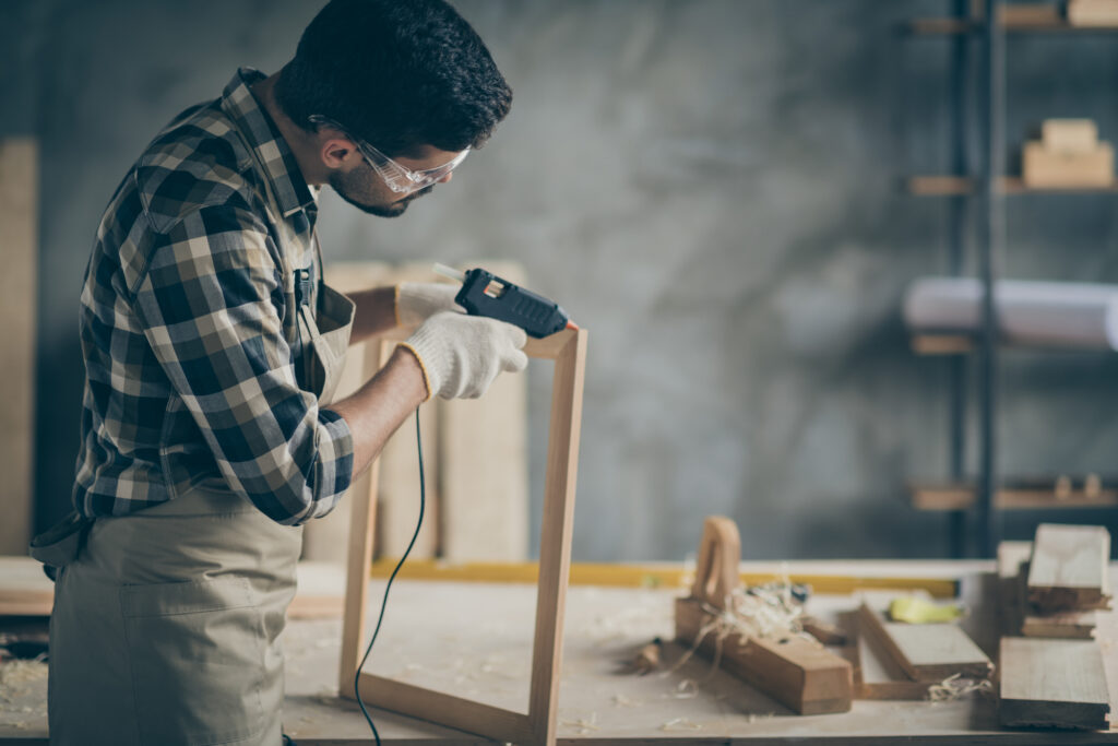 Profile side photo of serious concentrated worker man use electric, hot glue gun to repair wooden construction frame work in home house garage