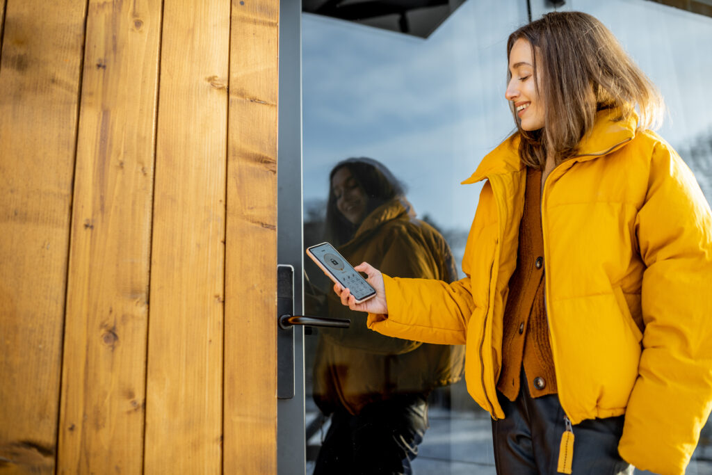 Woman locking smartlock on the entrance door using a smart phone. Concept of using smart electronic locks with keyless access