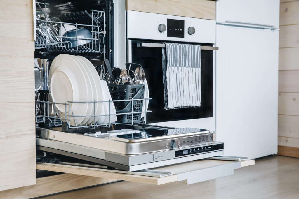 Open dishwasher with white clean dishes after washing in modern scandinavian kitchen. Clean kitchenware in open dishwashing machine.