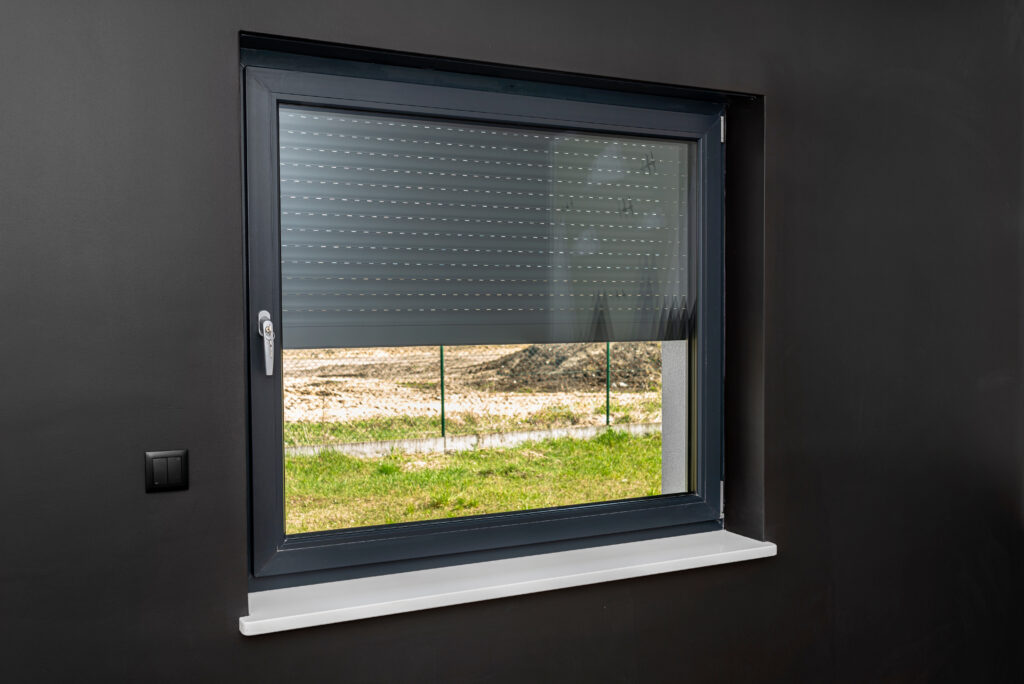 A large window in a room with black walls, half covered with external blinds.