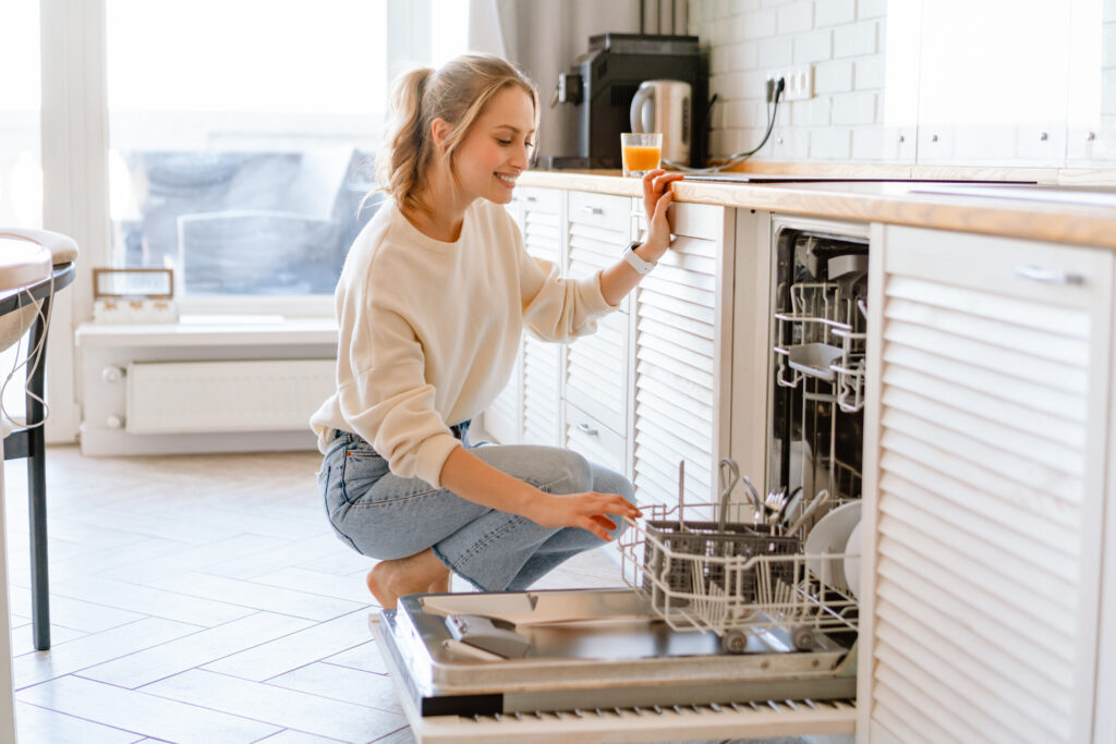 Smiling young white woman putting dishes in the dishwasher at home