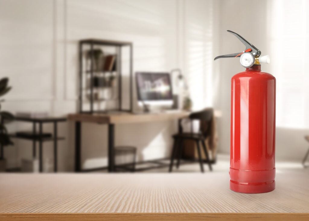 Fire extinguisher on wooden table in office. Space for text