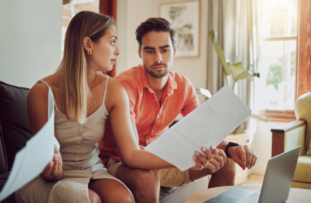 Unhappy, stressed and upset couple paying bills or debt online on with a laptop at home getting angry, planning budget. Young man and woman having a dispute over finance, savings and increasing tax.