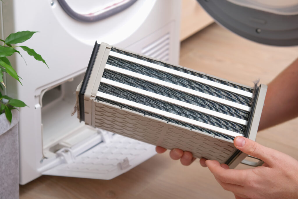 Drying machine with a full filter of lint, hair, dust, wool after the drying cycle of towels, bed linen. White drying machine. A man takes out a dirty radiator dryer.