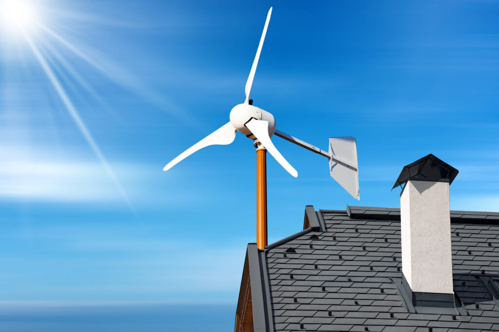 Close-up of a small wind turbine on the top of a roof of a house, against a blue sky with clouds and sunbeams. Renewable energy concept.