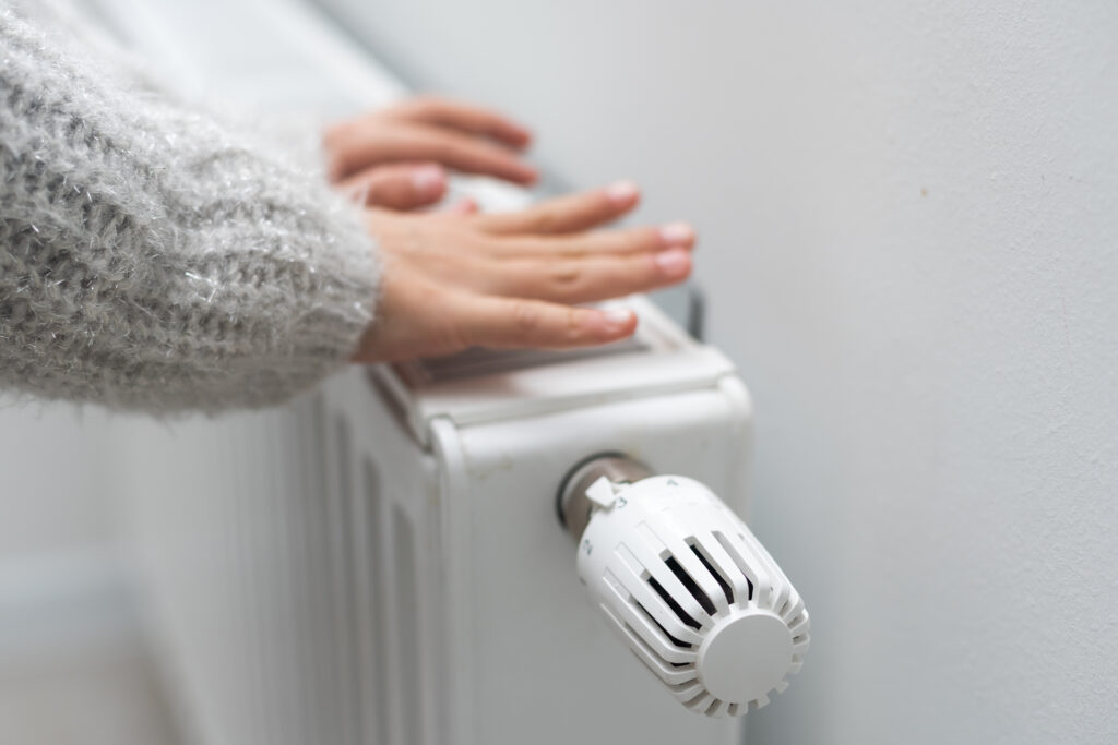 The child's hands warm their hands near the heating radiator. Saving gas in the heating season