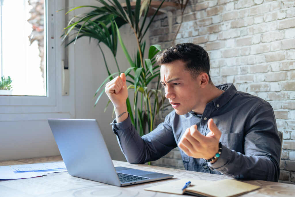 Unhappy young caucasian male worker in glasses look at laptop screen shocked by gadget breakdown or operational problems. Frustrated man confused surprised by unexpected error on computer device.