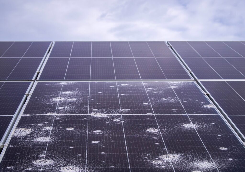 Close-up of a solar panel with visible hail damage, illustrating the impact of severe weather on renewable energy infrastructure and efficiency.