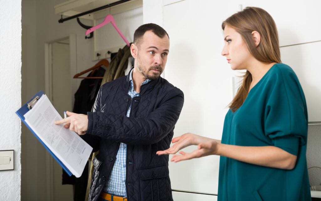 Portrait of young frustrated woman talking to debt collector visiting her at home and demanding to pay debts